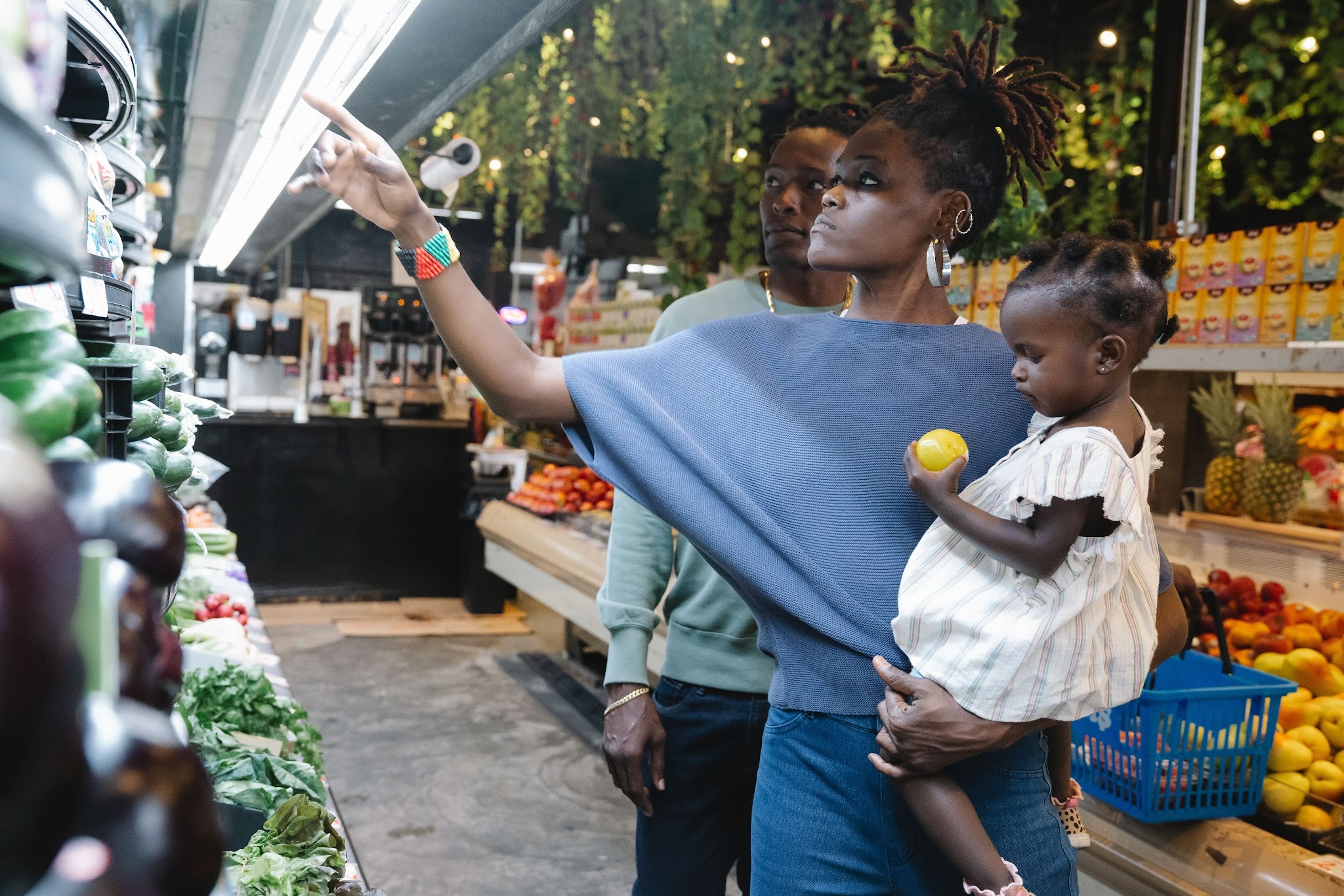 A man and a woman holding a small child shop for produce